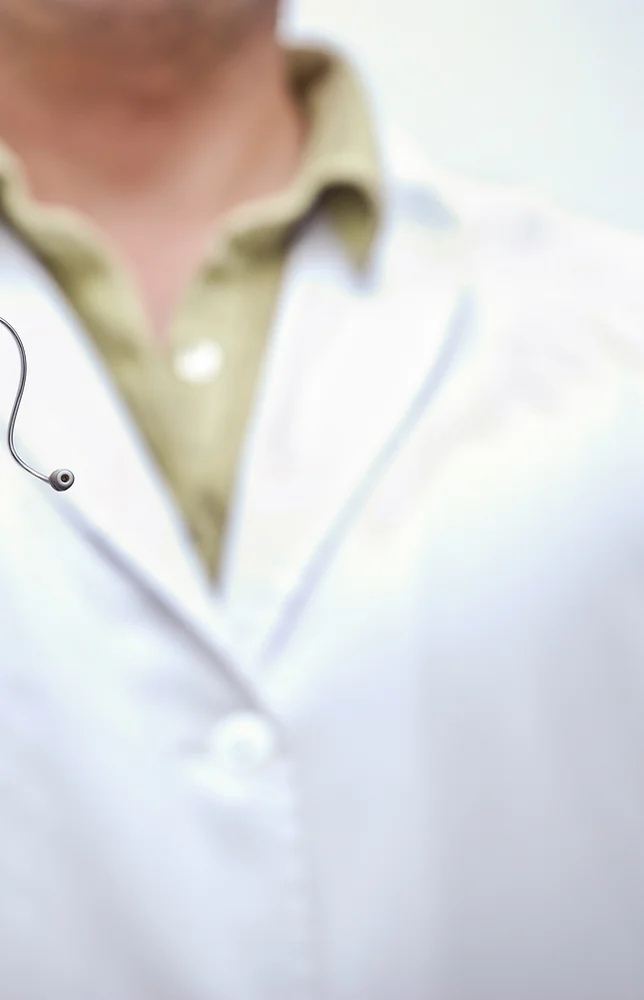 A man in a lab coat holds a hearing aid to display it.